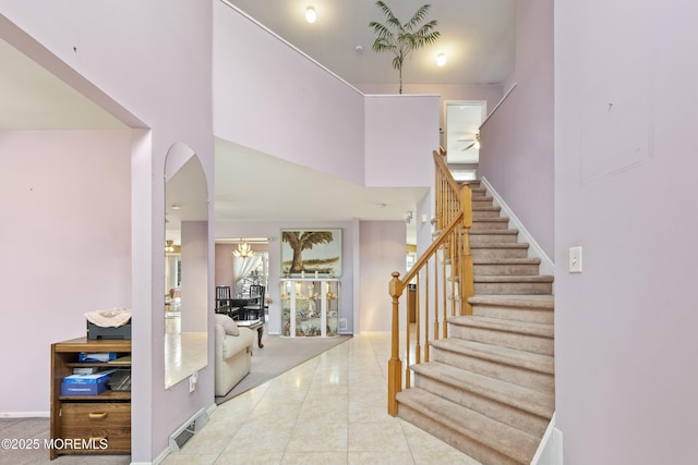 tiled foyer entrance featuring stairs, visible vents, arched walkways, and a towering ceiling