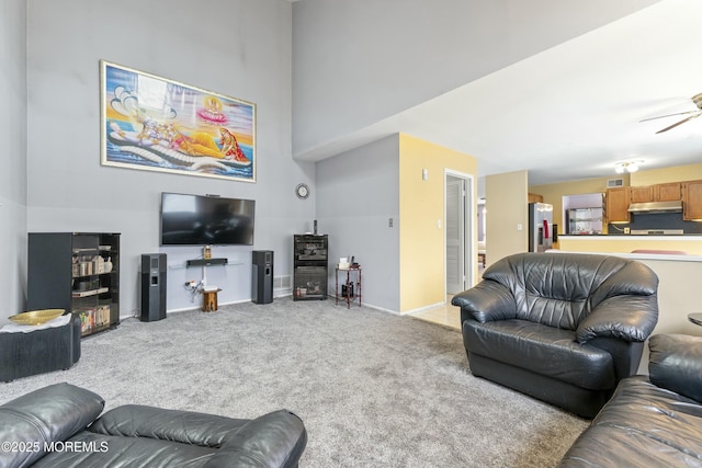 living area featuring light carpet, ceiling fan, a towering ceiling, and baseboards