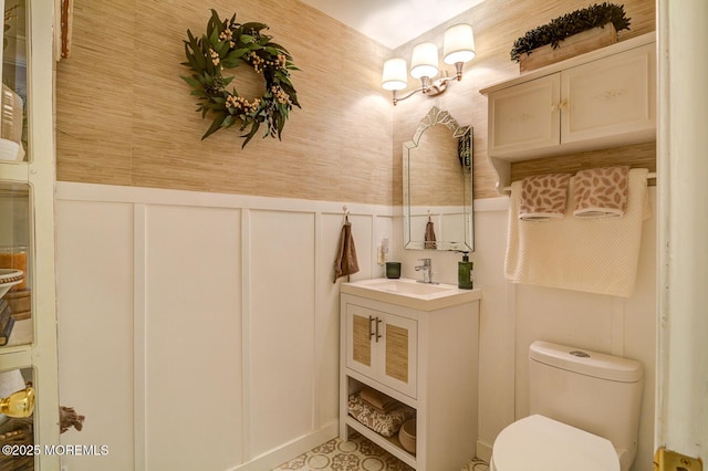 bathroom with vanity, a wainscoted wall, wallpapered walls, a decorative wall, and toilet