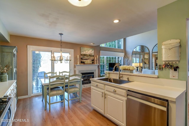 kitchen with a glass covered fireplace, white cabinetry, a sink, stainless steel dishwasher, and open floor plan