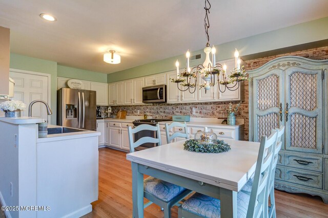 kitchen with decorative light fixtures, white cabinetry, stainless steel appliances, light wood finished floors, and decorative backsplash