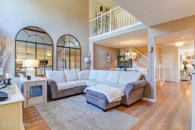 living room featuring wood finished floors, an inviting chandelier, baseboards, a towering ceiling, and stairs