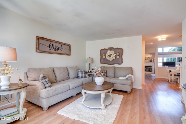 living area with a glass covered fireplace, visible vents, baseboards, and light wood-style flooring