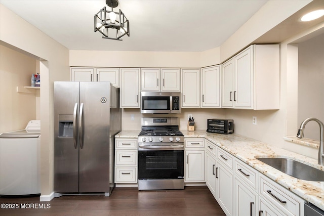 kitchen with light stone counters, stainless steel appliances, white cabinetry, a sink, and washer / dryer