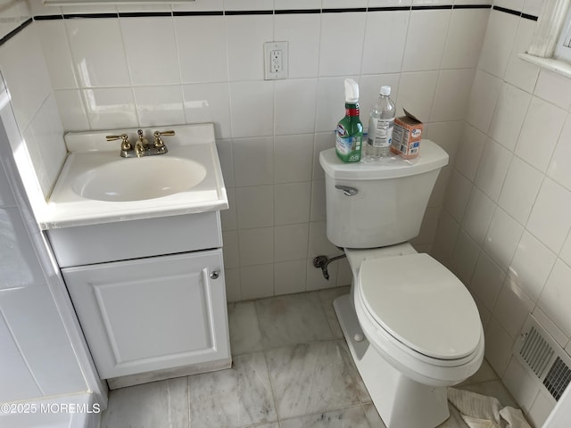 half bathroom with visible vents, toilet, vanity, and tile walls