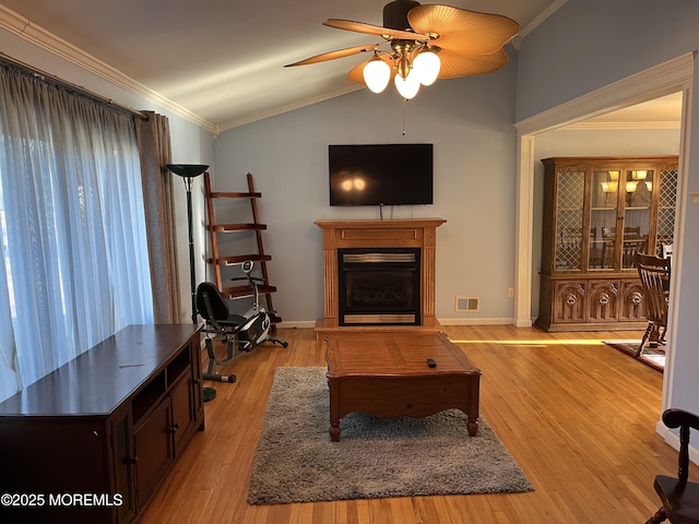 living room with crown molding, visible vents, a glass covered fireplace, vaulted ceiling, and light wood-type flooring