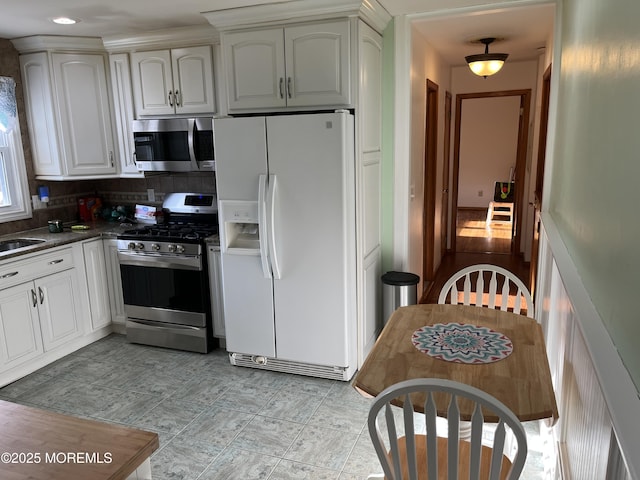 kitchen featuring stainless steel appliances, dark countertops, backsplash, white cabinets, and a sink