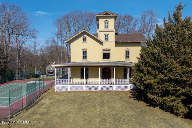 view of front of home featuring stucco siding, a porch, a tennis court, fence, and a front lawn