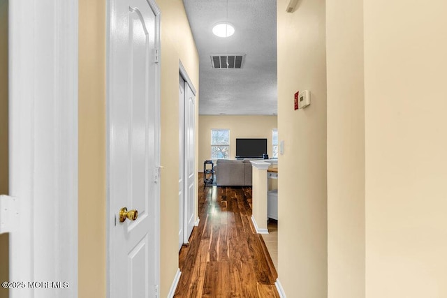 corridor featuring visible vents, dark wood finished floors, and a textured ceiling