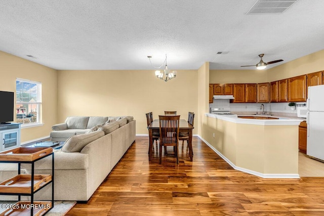 kitchen featuring brown cabinets, light countertops, open floor plan, a sink, and white appliances