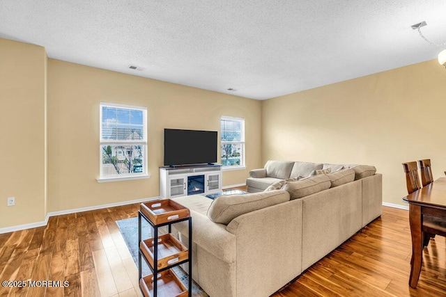 living area featuring a textured ceiling, wood finished floors, visible vents, and baseboards