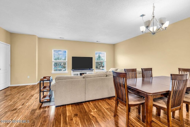 dining space featuring light wood-type flooring, a textured ceiling, baseboards, and a notable chandelier