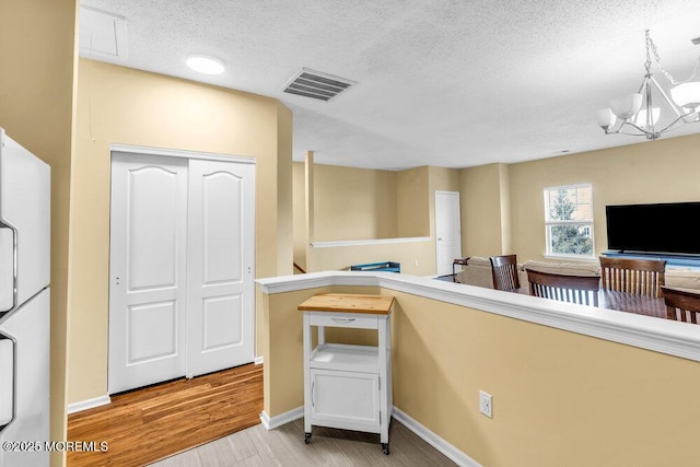 interior space with attic access, visible vents, a textured ceiling, light wood-type flooring, and a notable chandelier