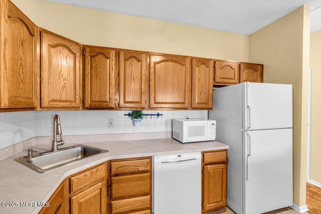 kitchen featuring brown cabinets, white appliances, light countertops, and a sink