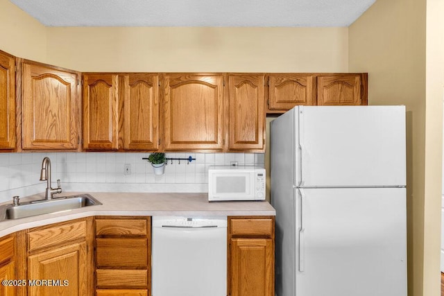 kitchen featuring brown cabinetry, white appliances, light countertops, and a sink