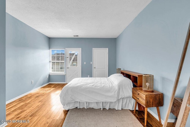 bedroom featuring light wood-type flooring, visible vents, baseboards, and a textured ceiling