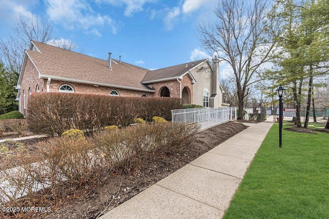 view of home's exterior with brick siding, a yard, a chimney, a shingled roof, and fence