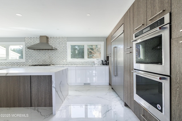 kitchen featuring white cabinets, marble finish floor, wall chimney range hood, appliances with stainless steel finishes, and modern cabinets