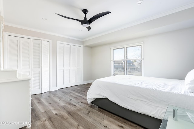 bedroom featuring ceiling fan, wood finished floors, baseboards, two closets, and crown molding