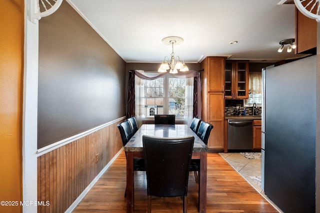 dining area featuring a wainscoted wall, light wood-style floors, ornamental molding, and an inviting chandelier