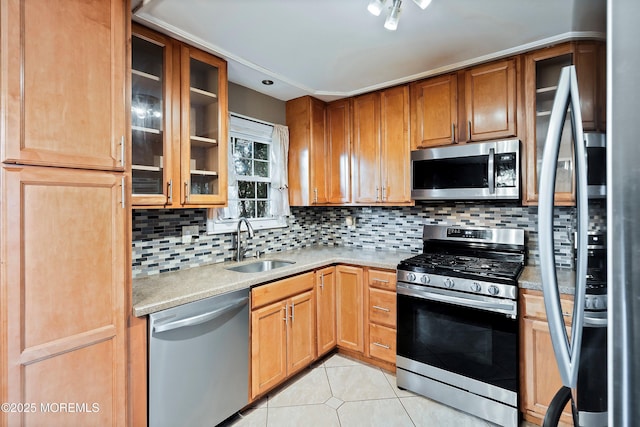 kitchen featuring glass insert cabinets, light countertops, stainless steel appliances, a sink, and light tile patterned flooring