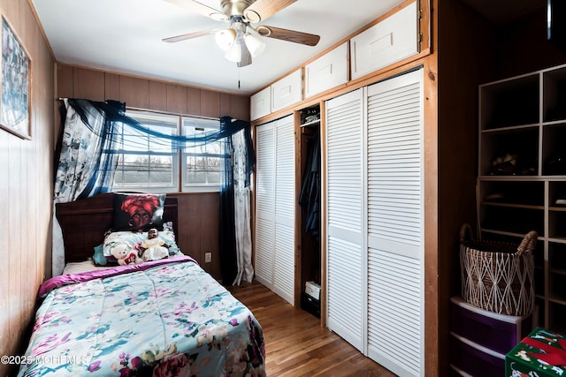 bedroom featuring a ceiling fan, wooden walls, and wood finished floors