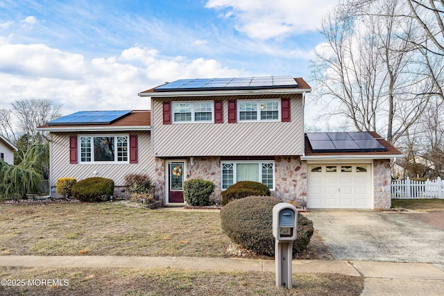 split level home with aphalt driveway, solar panels, fence, a garage, and stone siding