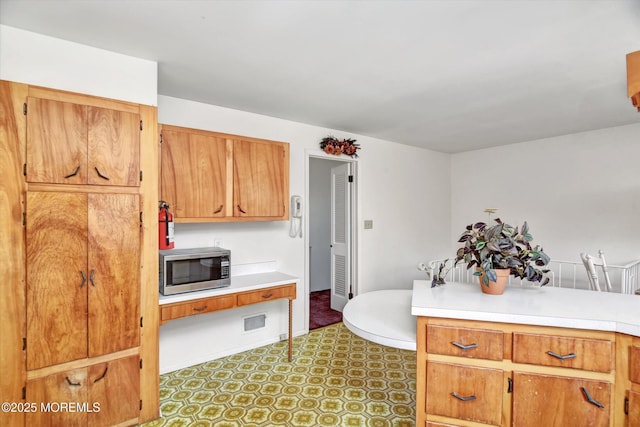 kitchen featuring tile patterned floors, visible vents, stainless steel microwave, brown cabinetry, and light countertops