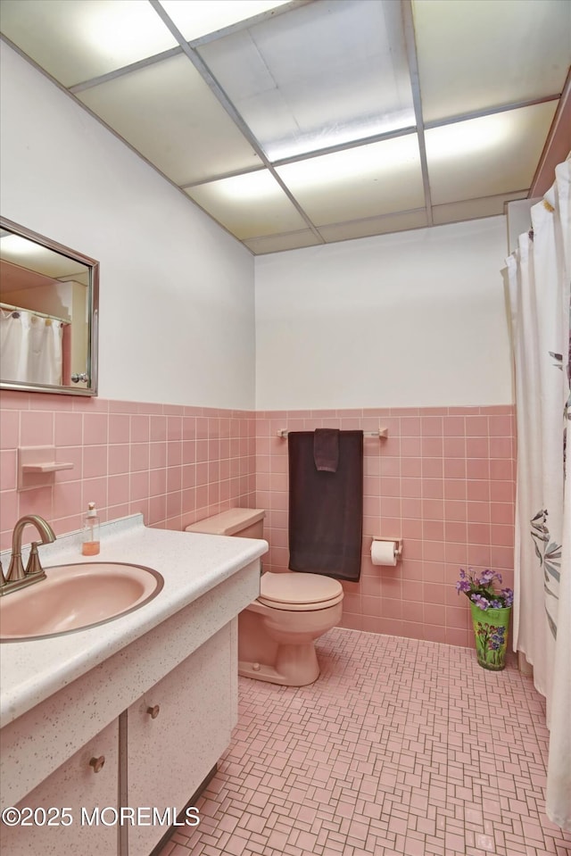 bathroom with tile walls, a wainscoted wall, toilet, a shower with curtain, and vanity