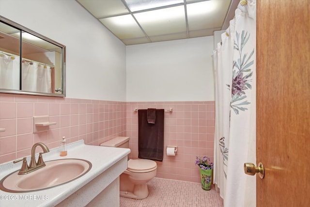 full bathroom featuring tile patterned flooring, tile walls, a wainscoted wall, toilet, and vanity