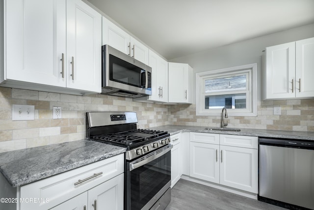 kitchen featuring light stone counters, tasteful backsplash, appliances with stainless steel finishes, white cabinetry, and a sink