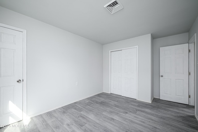 unfurnished bedroom with baseboards, a closet, visible vents, and wood finished floors