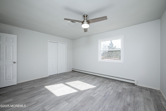 unfurnished bedroom with baseboards, visible vents, a baseboard radiator, wood finished floors, and a closet