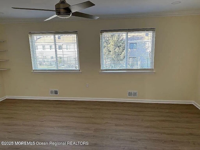 spare room with dark wood-style floors, visible vents, crown molding, and baseboards