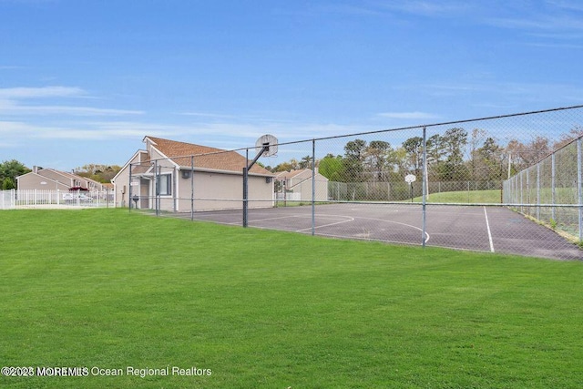 view of tennis court featuring community basketball court, fence, and a lawn