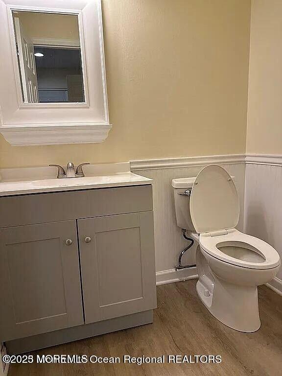 half bathroom featuring a wainscoted wall, vanity, toilet, and wood finished floors