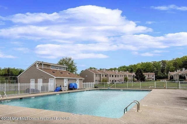 community pool with a patio area, fence, and a residential view