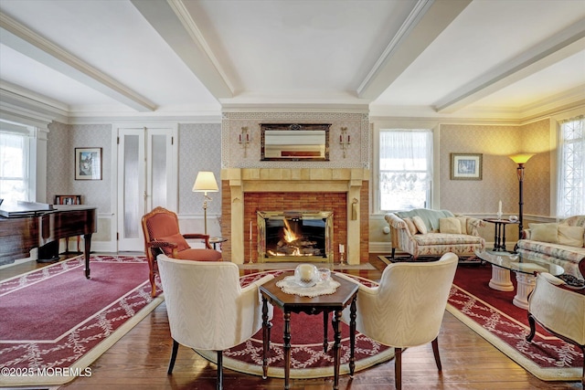 living area with a brick fireplace, a wealth of natural light, beam ceiling, hardwood / wood-style floors, and wallpapered walls