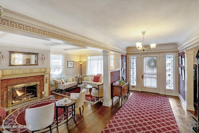 foyer with decorative columns, hardwood / wood-style flooring, a fireplace with flush hearth, ornamental molding, and a chandelier