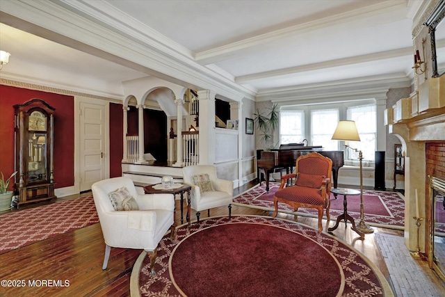 sitting room with baseboards, hardwood / wood-style flooring, beamed ceiling, crown molding, and a brick fireplace