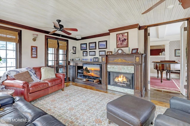 living room featuring wood finished floors, a ceiling fan, baseboards, a tiled fireplace, and crown molding