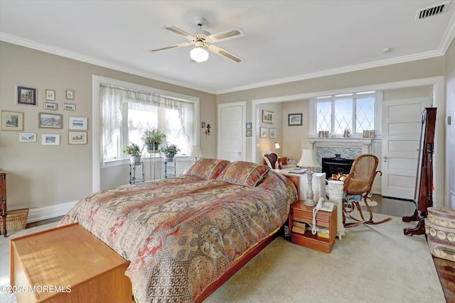 bedroom featuring a ceiling fan, visible vents, crown molding, and a lit fireplace