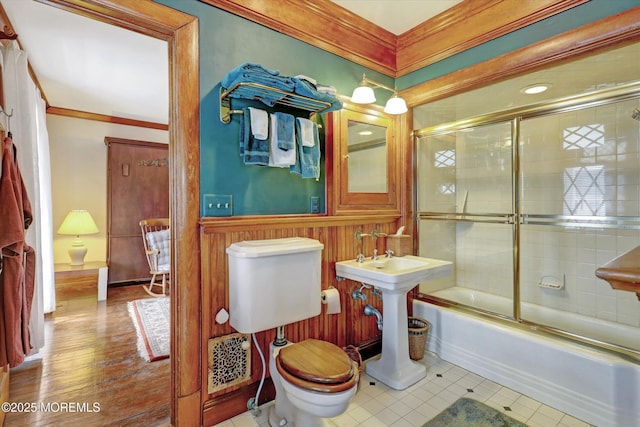 bathroom with toilet, a wainscoted wall, shower / bath combination with glass door, visible vents, and ornamental molding