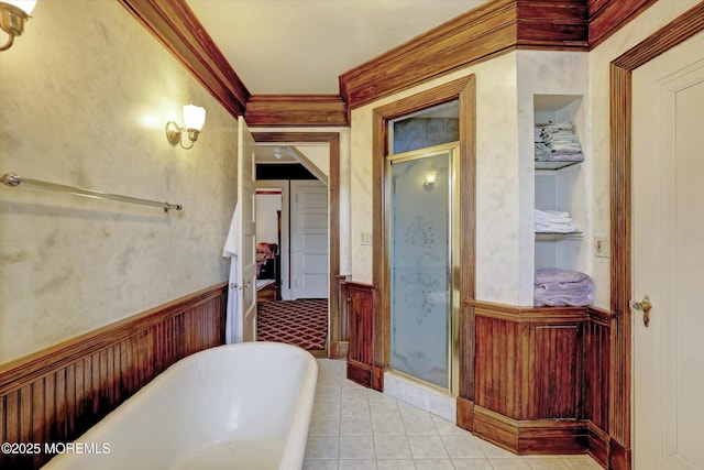 bathroom with a stall shower, a wainscoted wall, ornamental molding, tile patterned floors, and a freestanding bath