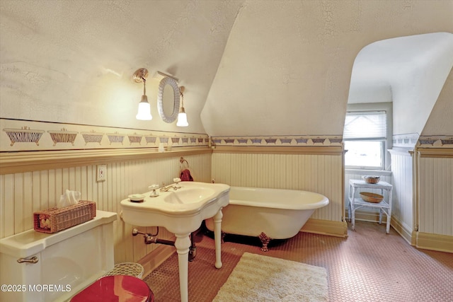 bathroom with a textured ceiling, a soaking tub, and wainscoting