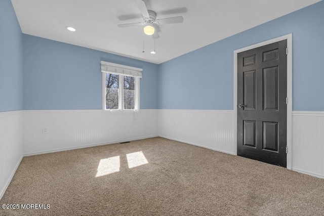 empty room featuring a wainscoted wall, carpet floors, and ceiling fan