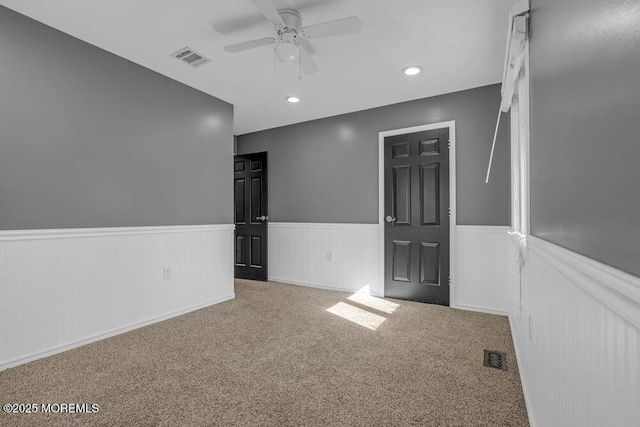 unfurnished room with a wainscoted wall, ceiling fan, visible vents, and carpet flooring