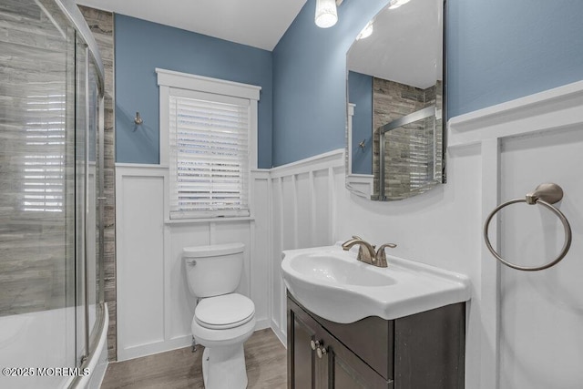 bathroom with toilet, a shower with door, vanity, and wainscoting