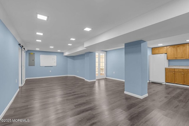 basement featuring a barn door, dark wood-type flooring, freestanding refrigerator, and baseboards