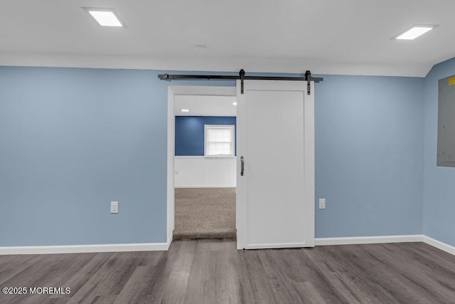 empty room featuring a barn door, baseboards, and wood finished floors